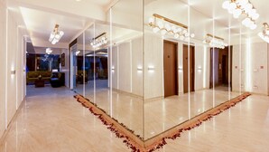 Un hall d’hôtel doté d’un grand miroir qui agrandit l’espace, d’un comptoir d’accueil et d’un coin salon avec un canapé et des fauteuils.