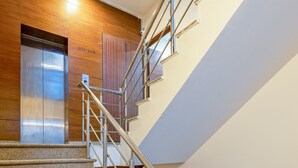 Un escalier moderne avec des rampes en métal et un mur en bois intégrant un panneau d’ascenseur.