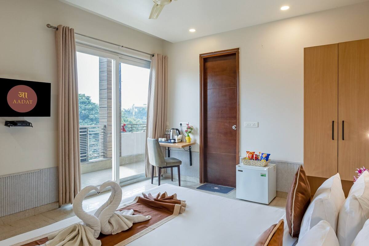 A hotel room with a bed, a desk, a chair, a television, a wardrobe, and a balcony with curtains.