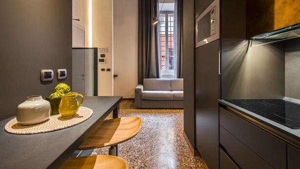 Une cuisine moderne dotée d’une cuisinière intégrée, un coin repas avec une table et des chaises en bois, et une vue sur le paysage urbain par une fenêtre.
