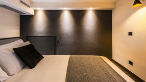 Une chambre d’hôtel moderne, équipée d’un lit, d’une tête de lit et d’un luminaire fixé au mur.