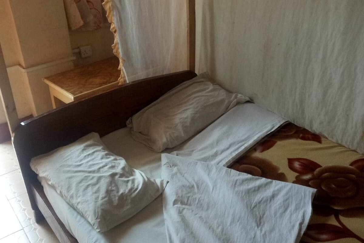 Un lit simple avec une literie blanche, une tête de lit en bois et une couvre-lit à motifs floraux.