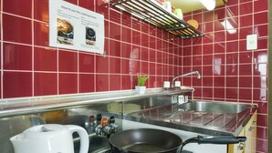 A kitchen with red tiled walls, a stainless steel sink, a stove, and a kettle. - PEOPLE NoIII 601 (Sapporo)