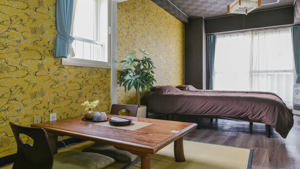 A hotel room with a wooden table, a bed, a potted plant, and a window with curtains. - PEOPLE NoIII 601 (Sapporo)
