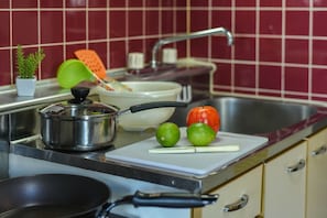 Una cocina con estufa, pileta y tabla de cortar con limones y un pimiento rojo.