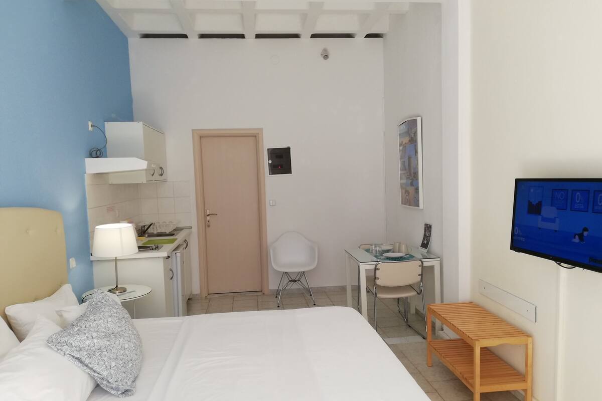 A hotel room with a bed, a desk, a chair, a TV, and a small wooden table.