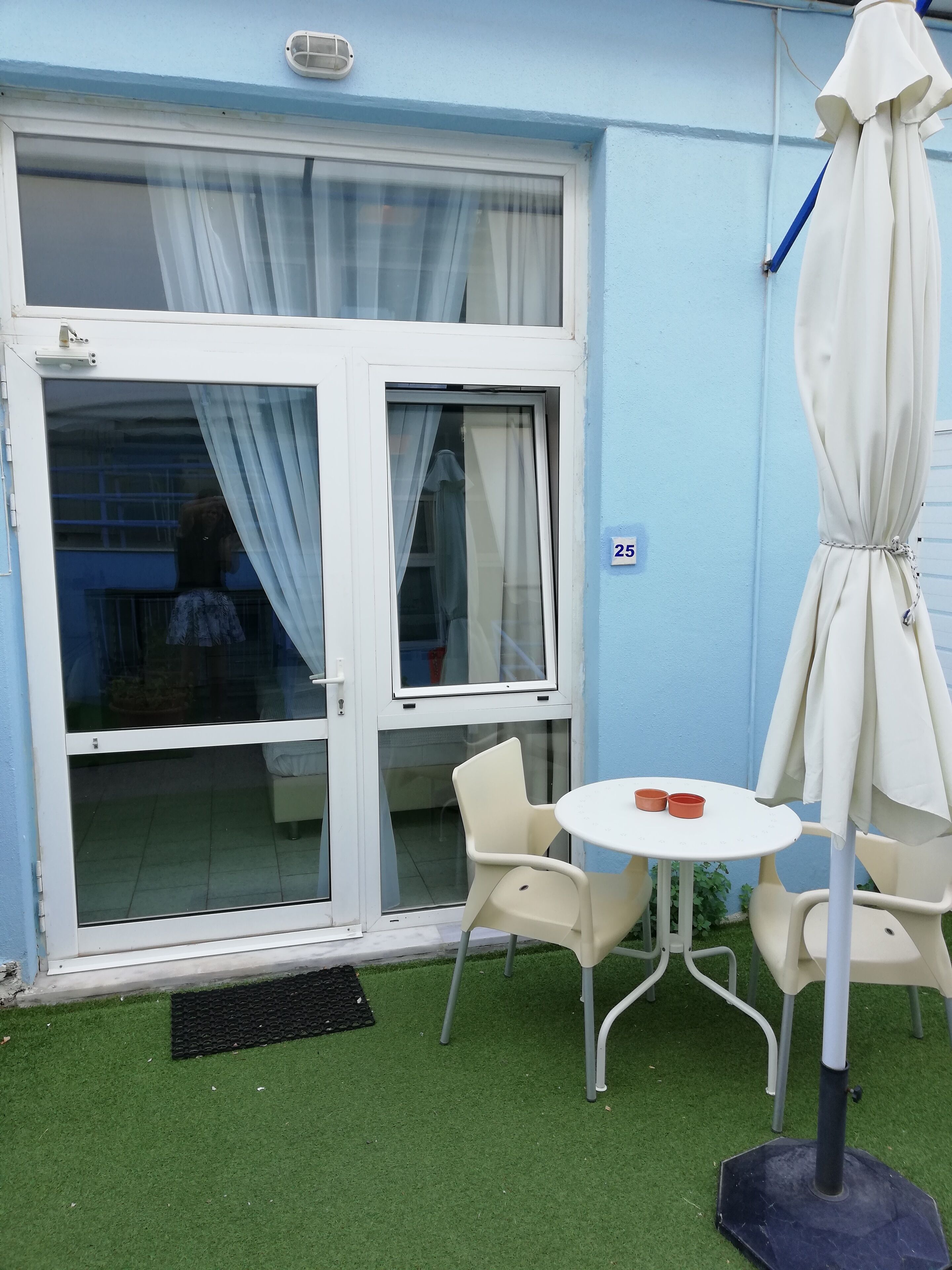 A patio with a white table and chairs, a white umbrella, and a sliding glass door with curtains.