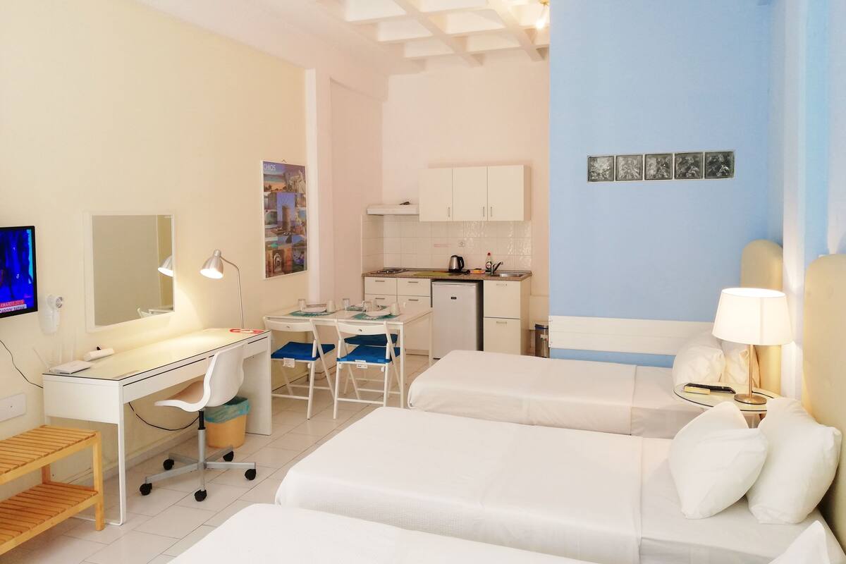 A hotel room with a desk, two beds, a small kitchenette, and a bathroom.