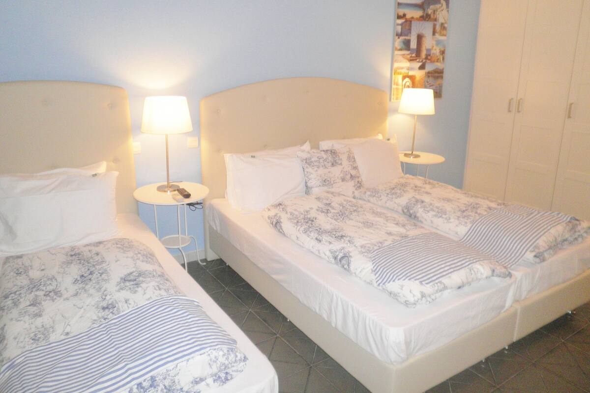 A hotel room with two beds, each with a pillow and a bedside table with a lamp.
