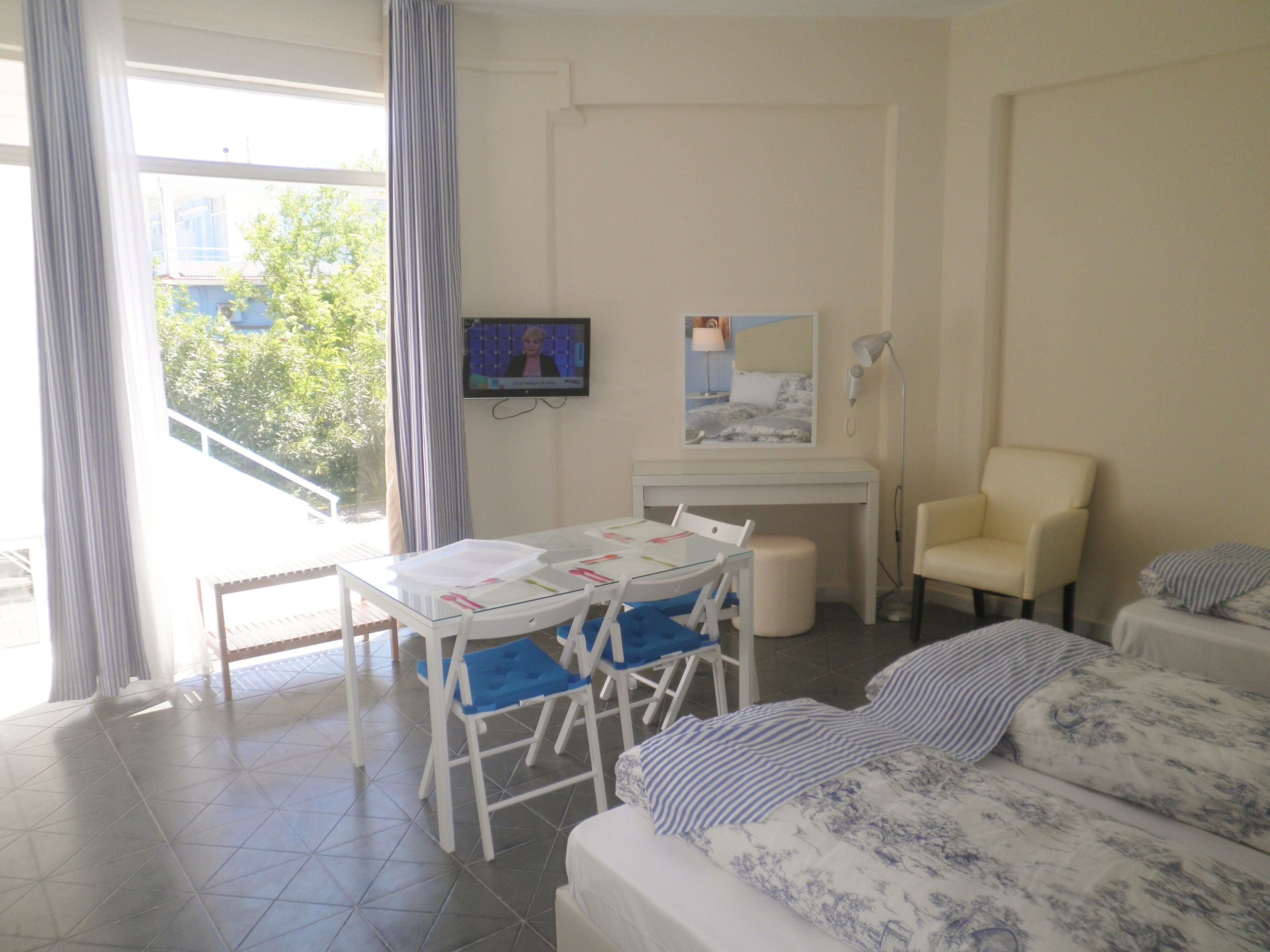 A hotel room with a bed, a desk with chairs, a television, a chair, and a view of the outdoors.