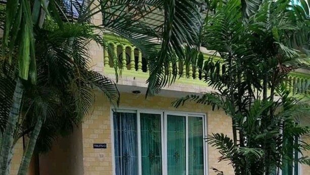 Un edificio con entrada de baldosas, un letrero que indica un baño, y un par de zapatos y una mochila en el suelo.