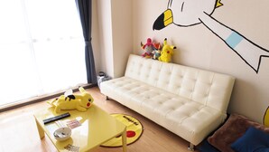 A living room with a white sofa, a yellow table with remote controls, and a Pikachu plush toy. - PEOPLE NoIII 810 (Sapporo)