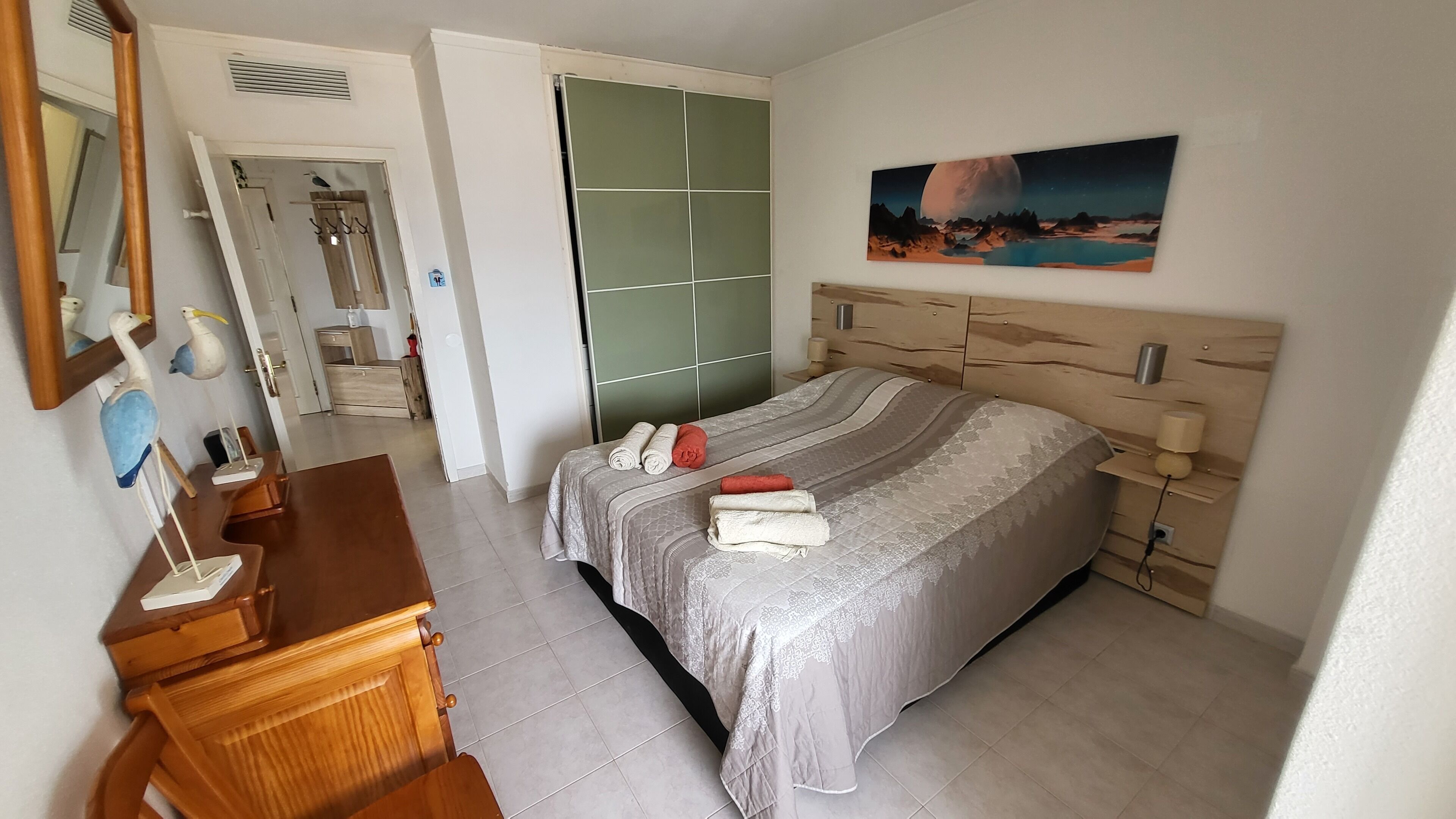 A bedroom with a bed, a dresser, a mirror, and a painting on the wall.
