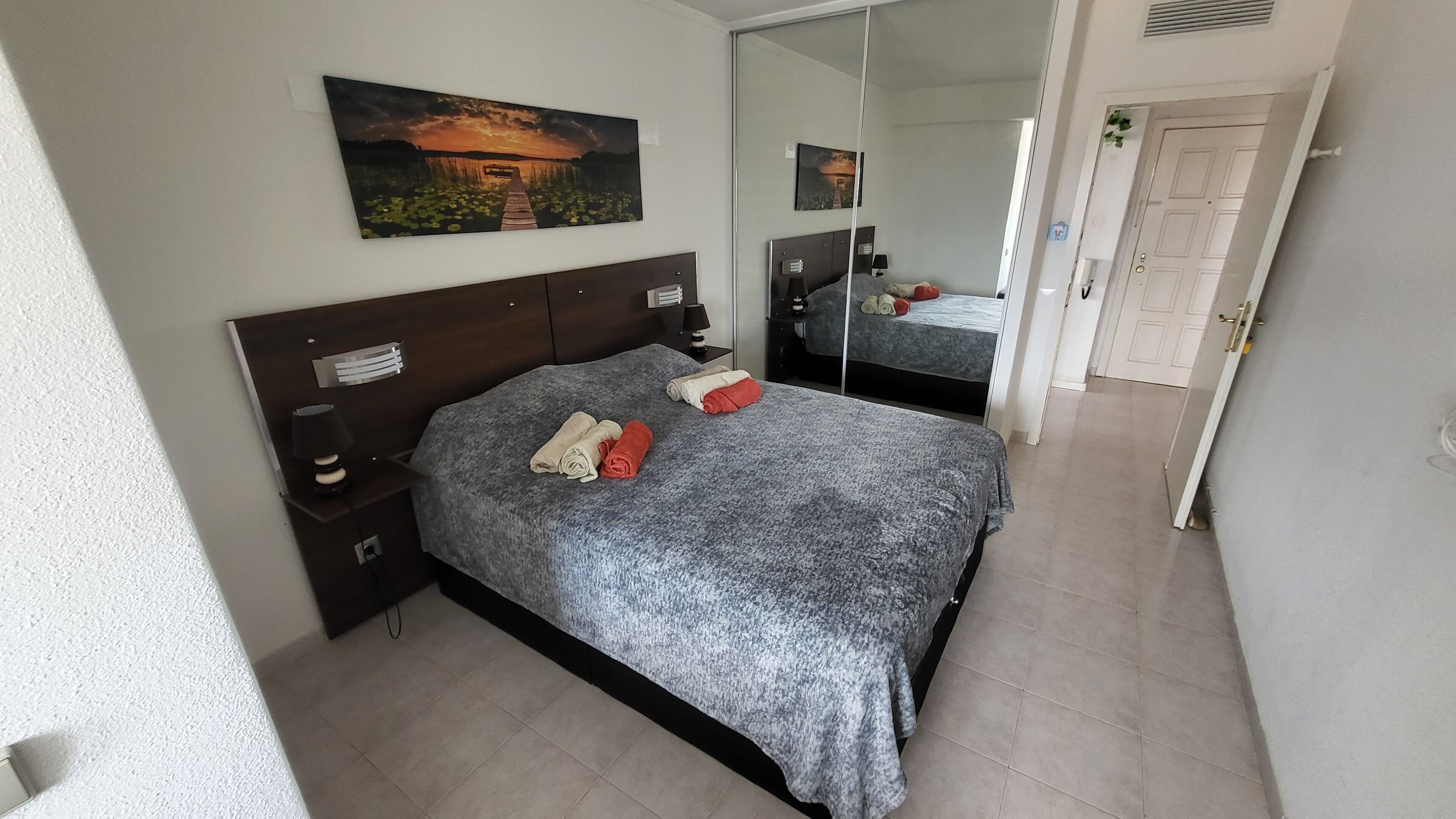 A neatly arranged bedroom with a bed, bedside tables, a mirror, and artwork on the wall.