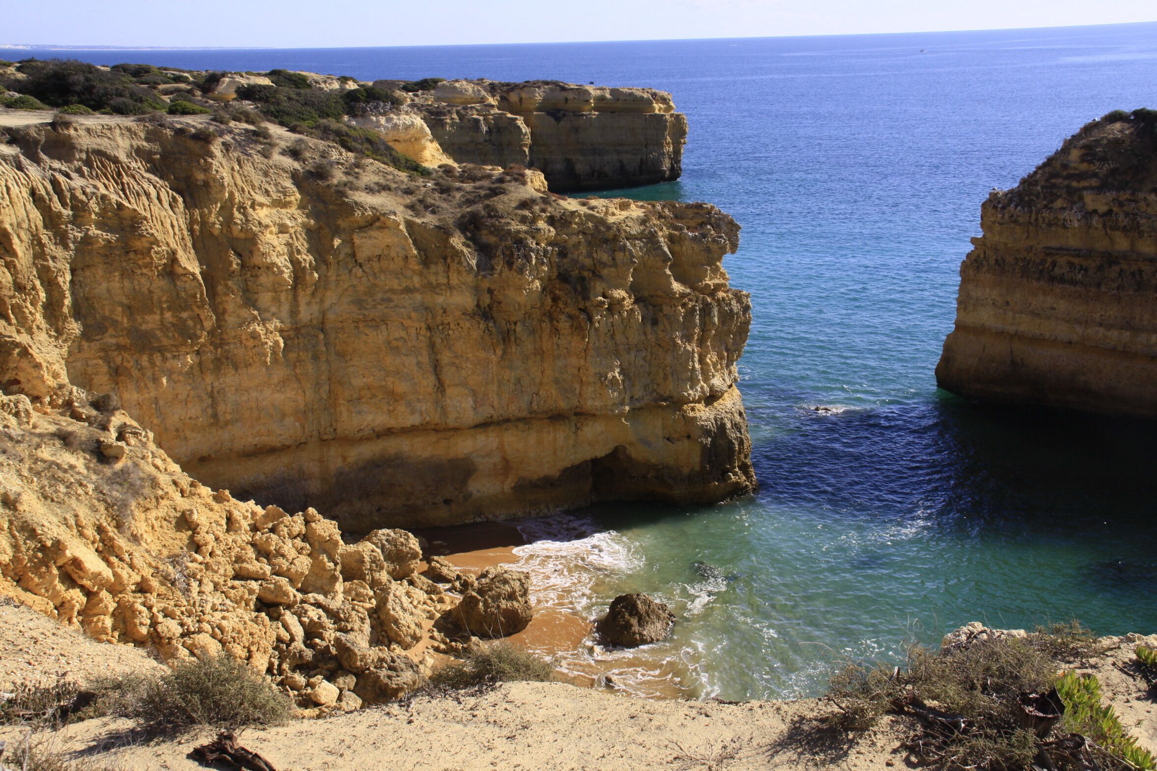 A coastal cliff with a rocky shoreline and clear blue sea.