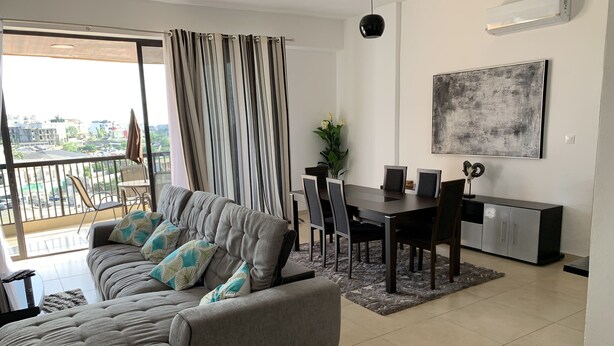 Ein modernes Wohnzimmer mit einer Couch, einem Esstisch, Stühlen und Blick auf die Stadt durch große Fenster.