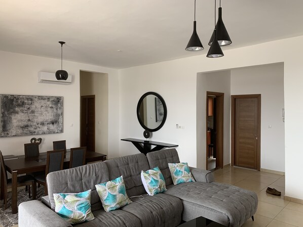 A modern living room with a grey sofa, a dining table, and a large abstract painting.