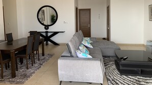 Ein modernes Wohnzimmer mit einem grauen Sofa, einem Esstisch und einem großen Spiegel.