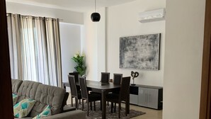 Ein modernes Wohnzimmer mit grauem Sofa, Esstisch, Stühlen und einem großen abstrakten Gemälde an der Wand.