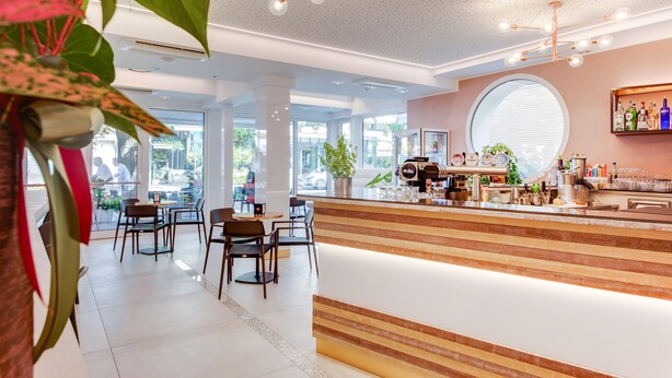 A modern bar area with a wooden counter, seating, and a large window. - Romagna Suite Hotel (Gatteo)