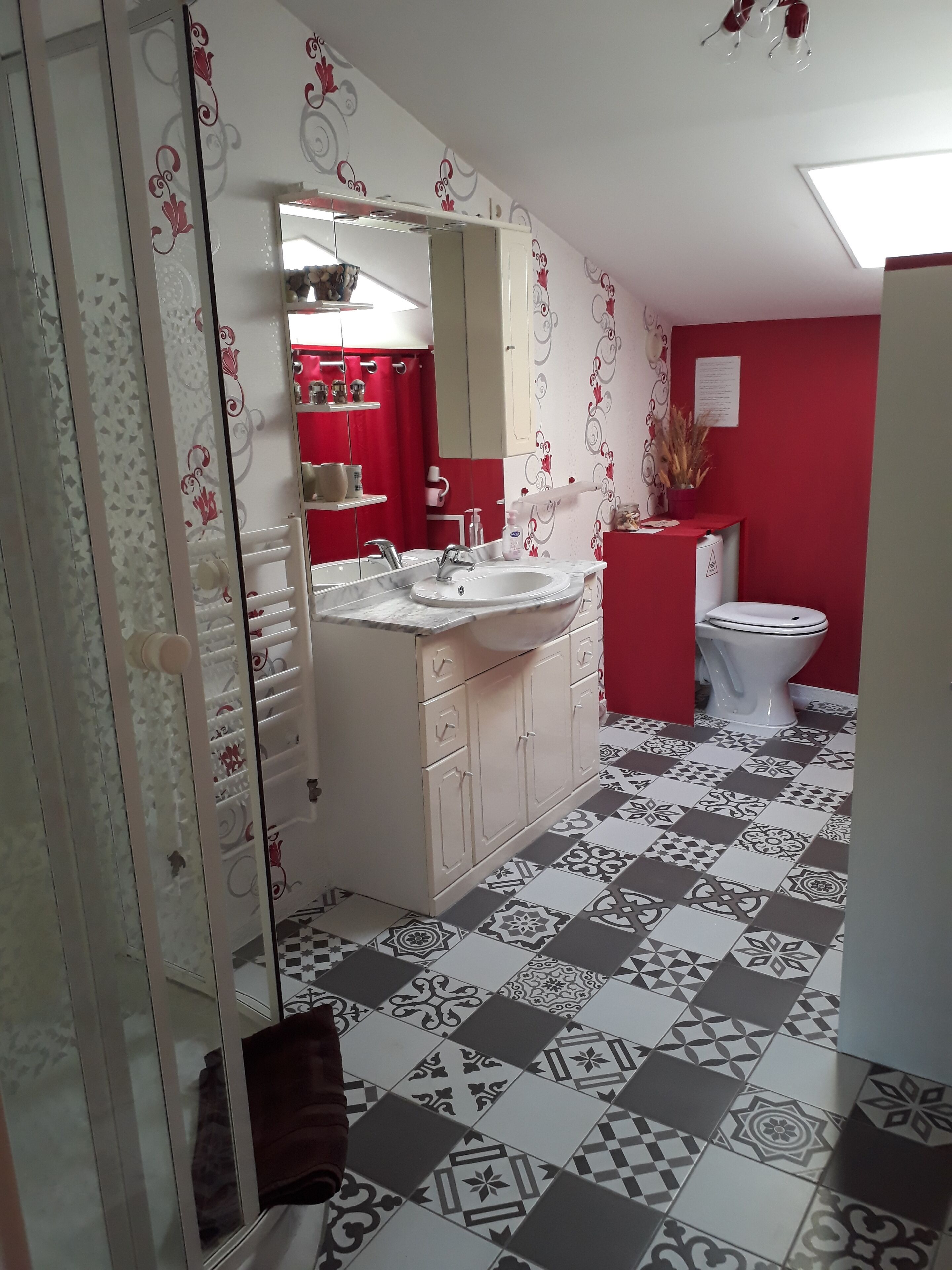Une salle de bain avec un lavabo blanc, un miroir et des toilettes, des murs rouges et des carreaux de sol à motifs.