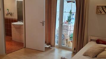 A bedroom with a bed, a window with curtains, a door leading to a bathroom, and a view of the outside.
