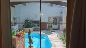 On aperçoit, à travers une porte vitrée, un jardin avec une piscine, des plantes en pot et un mur de briques.