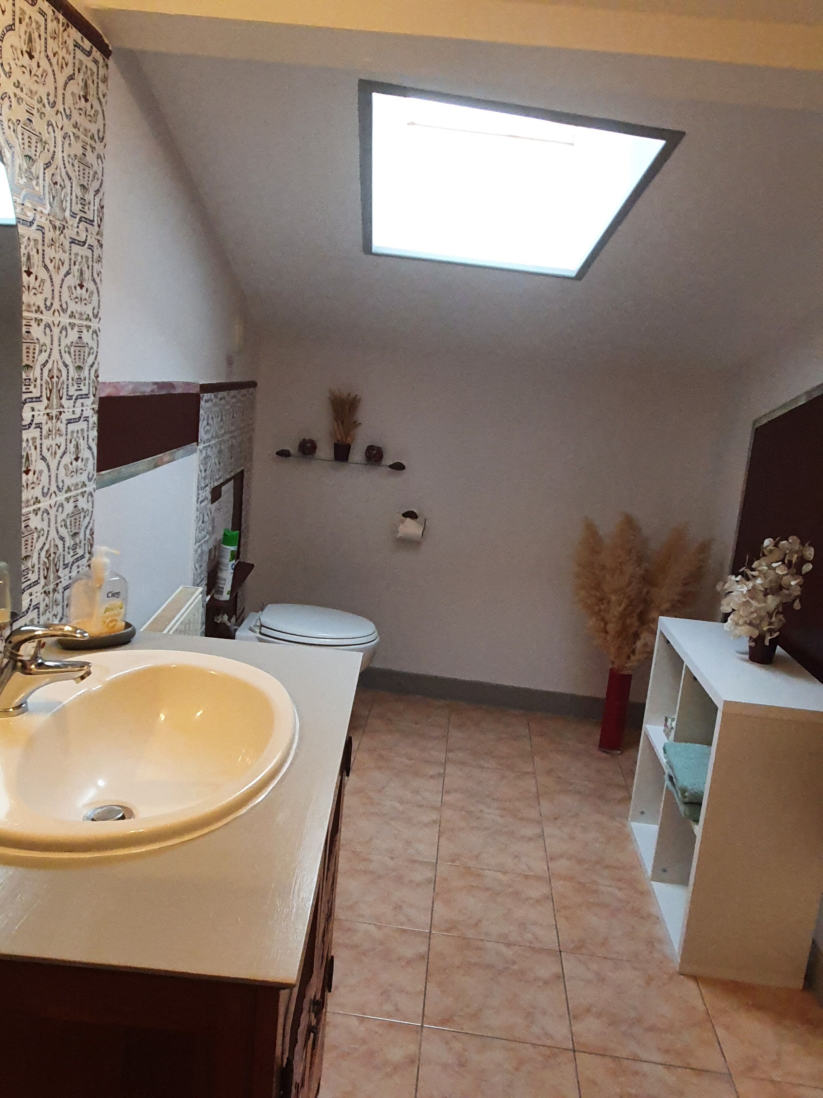 Un baño con un lavamanos blanco, inodoro y un estante pequeño con objetos decorativos.