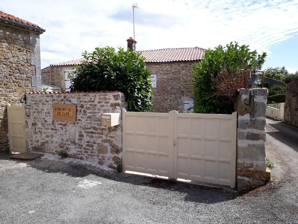 Une entrée fermée par un portail, avec un mur en pierre et une enseigne indiquant : « LE RUIT DE LA CURE ».