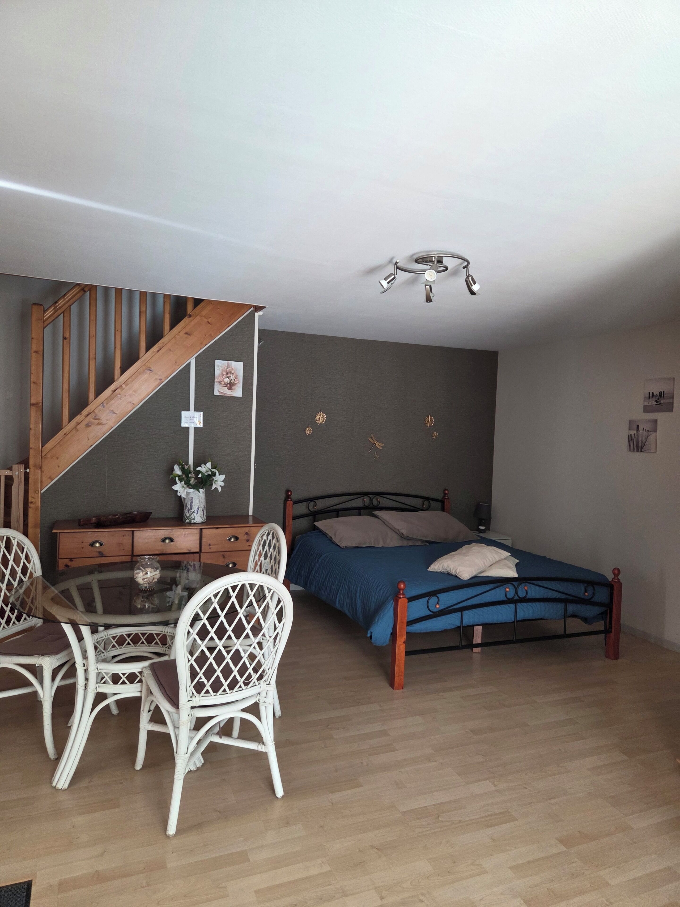 Um quarto com uma cama, uma cômoda de madeira, uma mesa de vidro com cadeiras e uma escada.