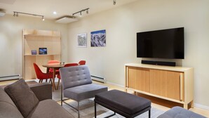 A modern living room with a grey sofa, a grey armchair, a red dining table with red chairs, a wooden cabinet with a flat-screen TV, and artwork on the wall. - Downtown Carbondale Retreat Next to Sopris Park, Walkable & Dog-Friendly (Carbondale)