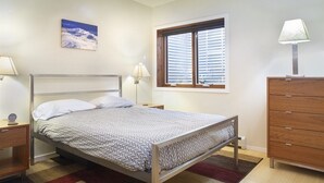 A bedroom with a bed, bedside lamps, a wooden dresser, a window with blinds, a ceiling fan, and a wall-mounted picture. - Downtown Carbondale Retreat Next to Sopris Park, Walkable & Dog-Friendly (Carbondale)