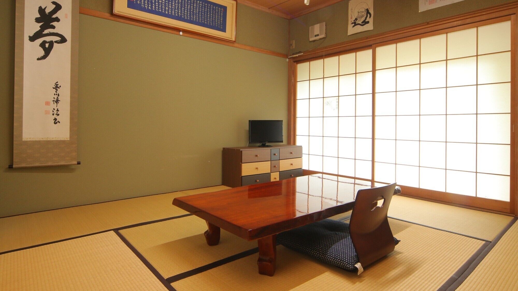A traditional Japanese room with tatami flooring, a low wooden table, a television on a cabinet, and shoji screens.