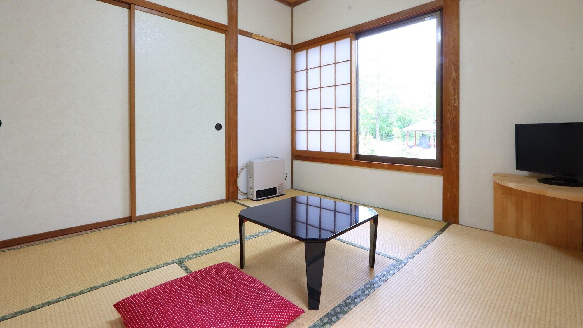 A traditional Japanese room with tatami flooring, a low table, a television, and a heater.