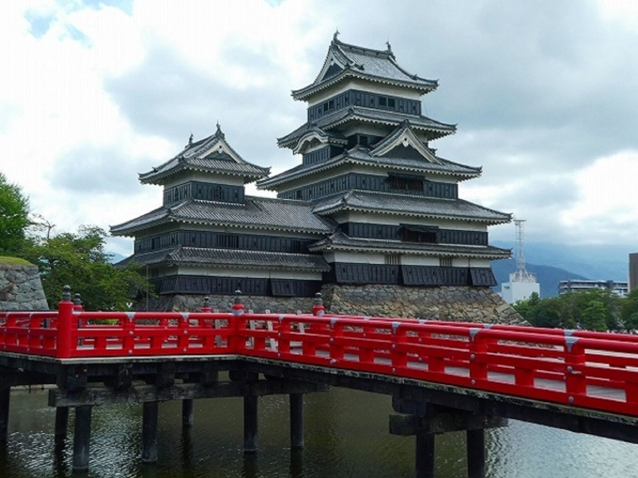 Eine traditionelle japanische Burg mit mehreren Ebenen und einer roten Brücke, die dorthin führt.