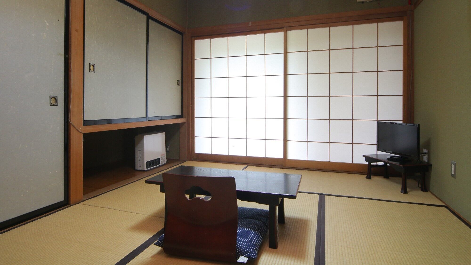 A tatami mat room with a low table, a chair, a television, and a cabinet.