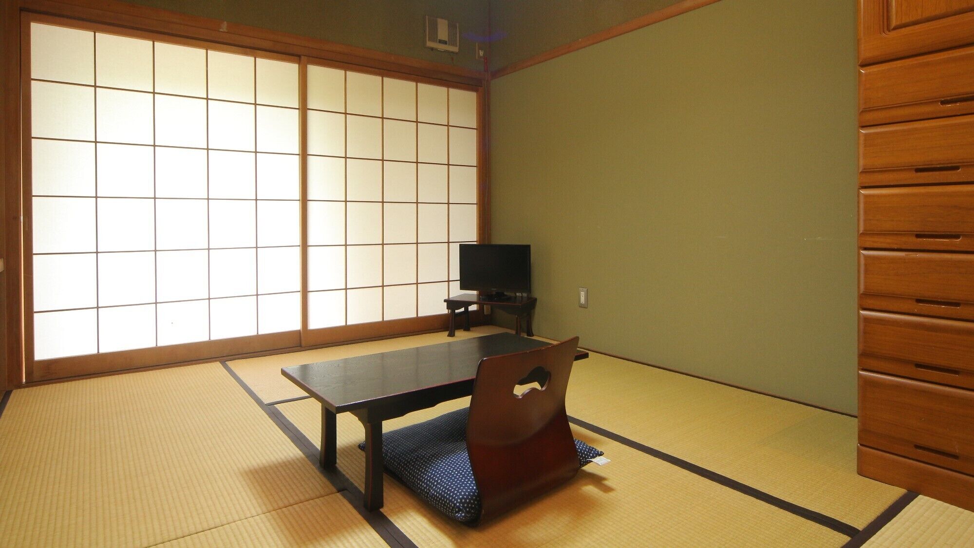 A tatami mat room with a low table, a television, and a wooden cabinet.