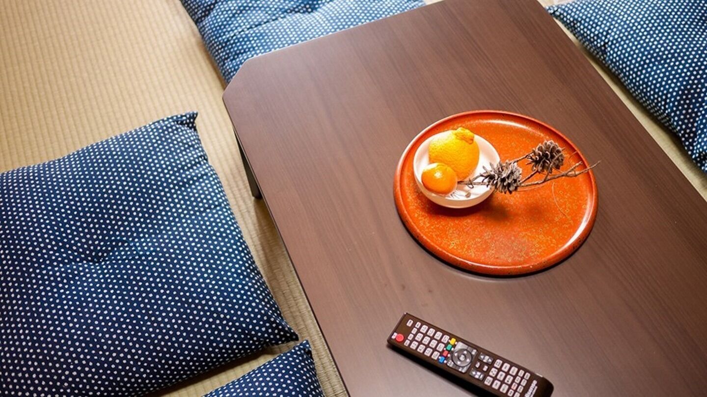 A room with a wooden table, a remote control, and a plate with a lemon and pine cones.