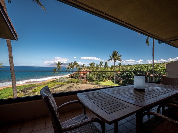 A balcony with a view of the beach, palm trees, and a mountain in the distance.