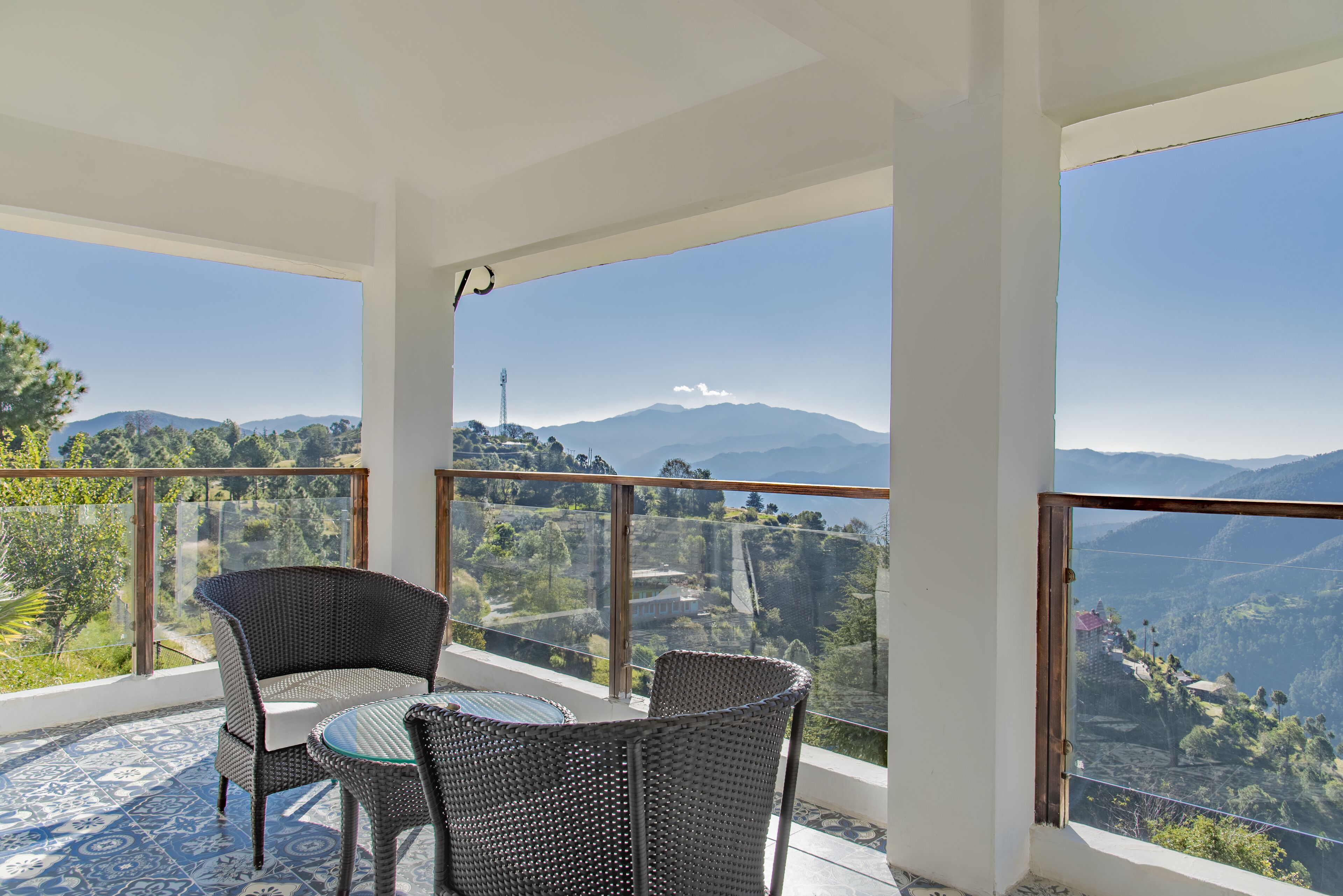 A balcony with wicker furniture and a clear view of mountains and a tower.