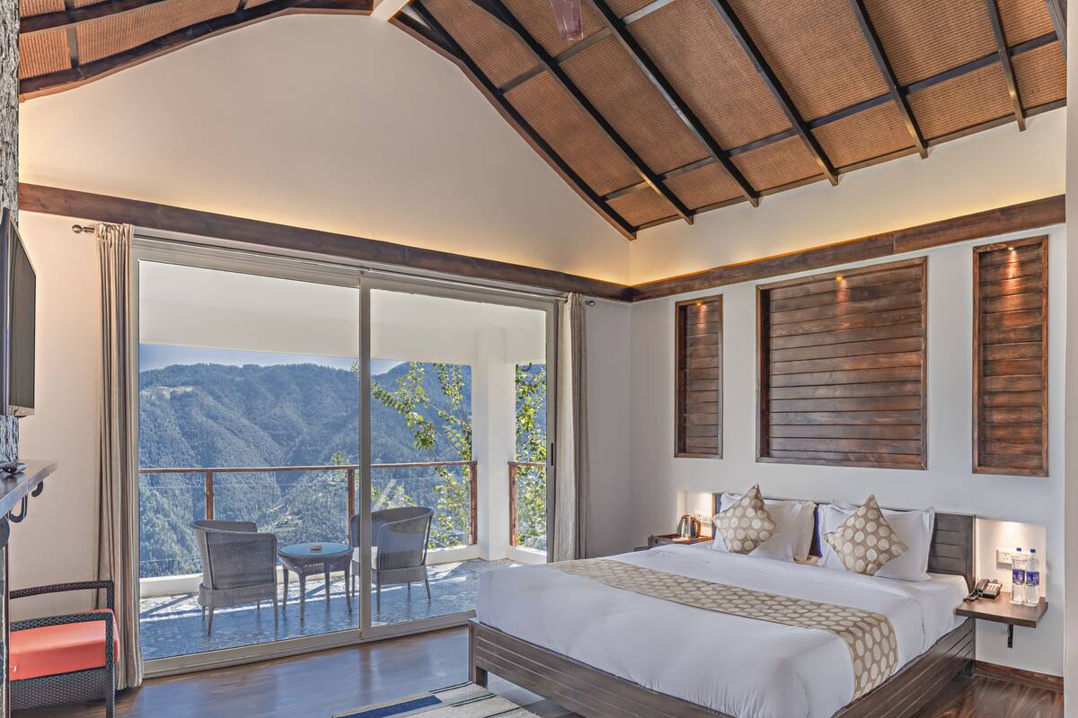 A bedroom with a large bed, a balcony with a view of mountains, and a television on a stand.
