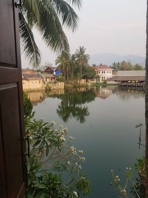 A calm water body with reflections of palm trees and buildings, surrounded by greenery and a few structures with red roofs.