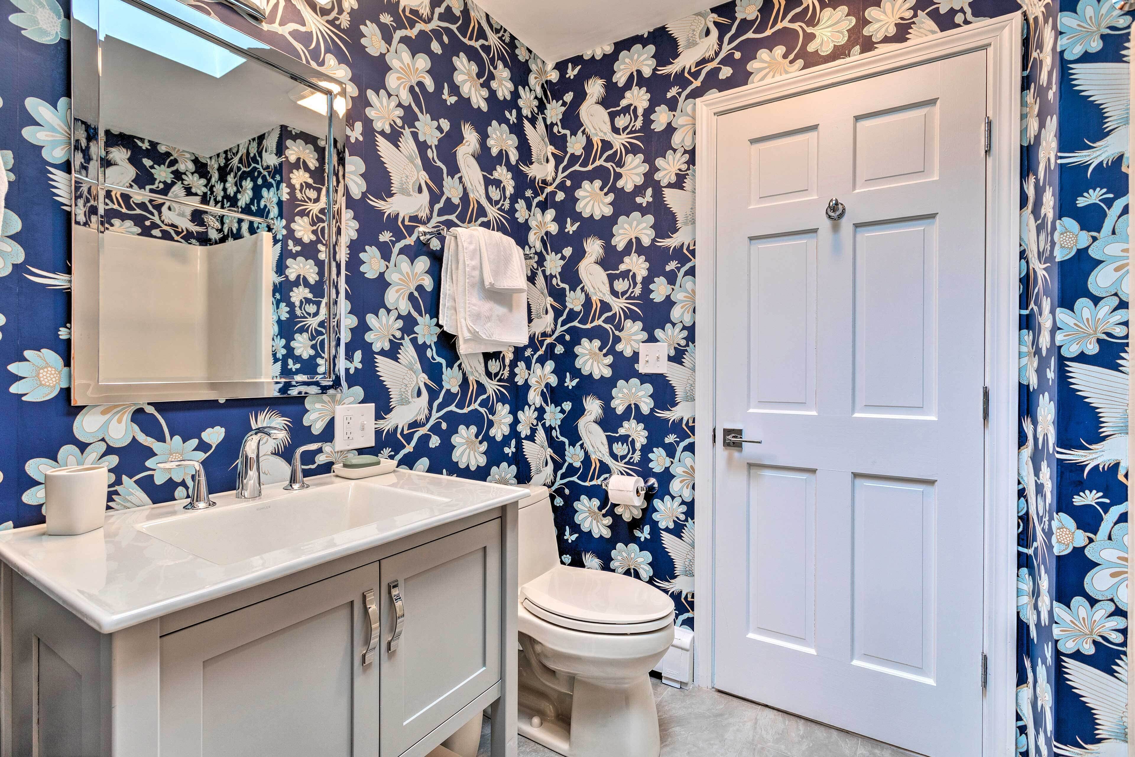 A bathroom with a white sink, mirror, and toilet against a blue floral wallpaper.