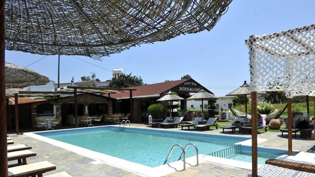 A pool area with lounge chairs and umbrellas, a pool bar, and a building with a sign reading "Borsallino". - Yalis Studios (Skiathos)