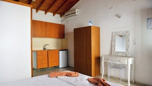 A bedroom with a bed, a wooden wardrobe, a small kitchenette, and a white vanity with a mirror. - Yalis Studios (Skiathos)