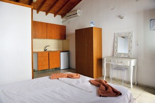 Un dormitorio con cama, un armario de madera, una pequeña kitchenette y un tocador blanco con espejo.