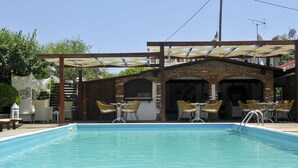 A swimming pool with outdoor seating and a covered patio area. - Yalis Studios (Skiathos)