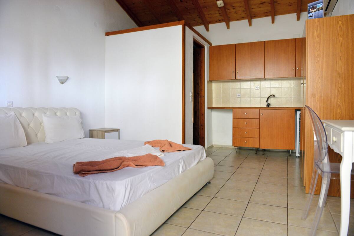 A bedroom with a large bed, a small bedside table, and a bathroom with wooden cabinets and a sink.