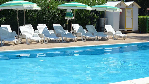 A swimming pool with white lounge chairs and green umbrellas. - Pozzo al Moro Village (Campo nell'Elba)