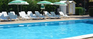 En pool med vita solstolar och gröna parasoller.